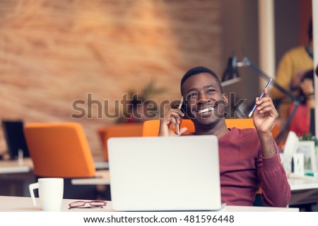 African American businessman on the phone sitting at the computer in his startup office Royalty-Free Stock Photo #481596448