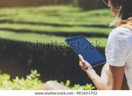 Hipster girl with backpack, sunglasses and vintage photo camera using tablet computer, copy space of blank mockup, tourist hands holding gadget and texting message on device on background sun flare