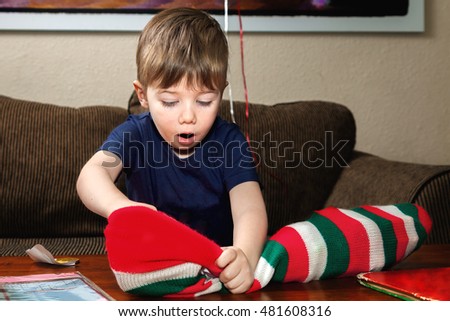 A little boy digs into his Christmas stocking with a look of excitement and wonder on his face.