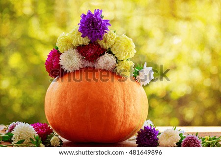 Pumpkin with colorful flowers on wooden table against natural background