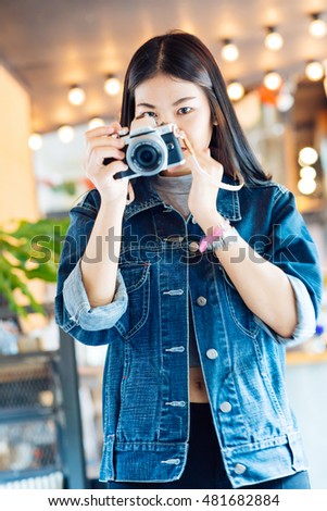 Young photographer woman wear jean cloth smiling in vintage coffee shop with mirrorless camera leather strap