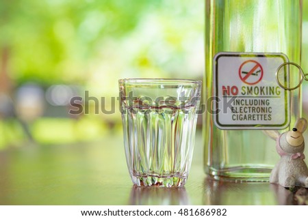 a glass and No smoking sign with green background nature on wooden table.
