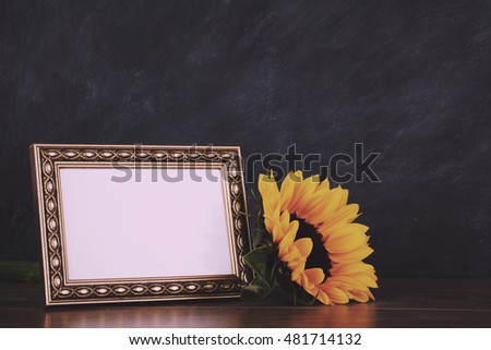 Old picture frame and sunflower against a dirty blackboard background Vintage Retro Filter.