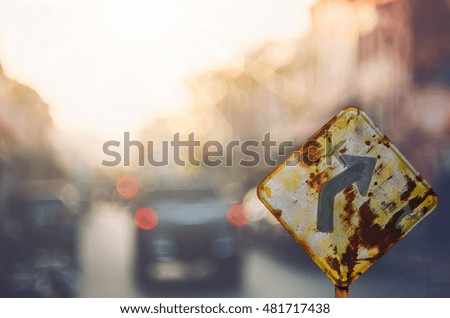 Old curve road warning sign on blur traffic road with colorful bokeh light abstract background. Copy space of transportation and travel concept. Retro tone filter color style.