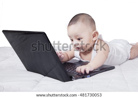 Picture of a cute male baby lying on the bed while playing laptop, isolated on white background