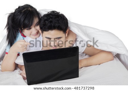 Photo of two Asian couple relaxing on the bed while using laptop computer together