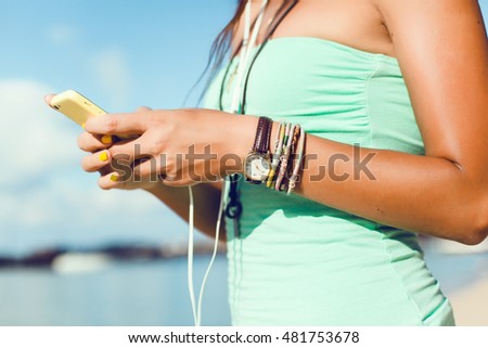 Young pretty brunette woman posing in the beach, listening music in smartphone player, smile, happy face, hipster style, outdoor portrait, reading text, message, sunglasses, close up, sea, Thailand,