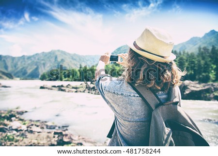 Young woman traveler on a background of mountains takes photos on a mobile phone. Travel concept.  Image with retro filter.
