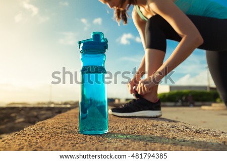 Drinking water concept. Female runner tying her shoe next to bottle of water.  Royalty-Free Stock Photo #481794385