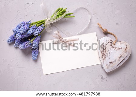 Bunch of blue spring muscaries flowers, decorative heart  and empty tag on textured grey background. Selective focus. Place for text. 