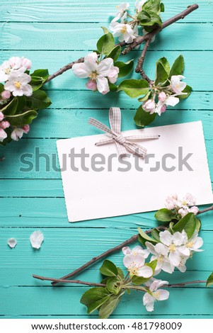 Empty tag and apple tree flowers on turquoise  wooden background. Selective focus. Place for text.