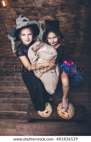 Children girls costumes witches with pumpkins and treats in the Halloween on wooden background scenery