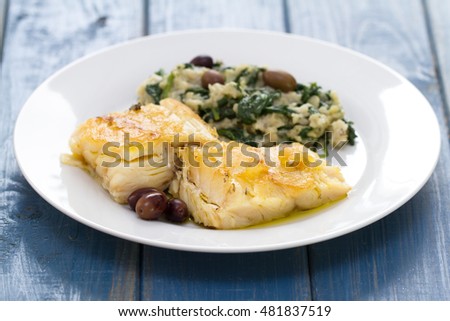 fried codfish with bread and spinach on white plate on white wooden background