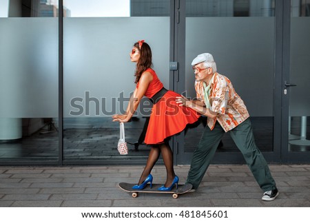 Old man pushing a woman on a skateboard.