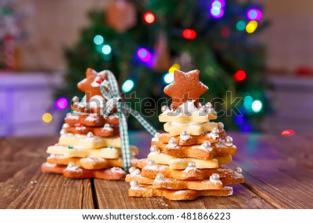 Home made baked Christmas gingerbread tree as a gift for family and friends on wooden background. With colorful lights from Christmas tree on background. With icing sugar as snow. 