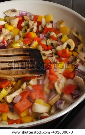 Frying or sauteing process.  A mixture of fresh vegetables in a ceramic pan on cooker hob with wooden spatula.  Rising steam visible at front of pan.