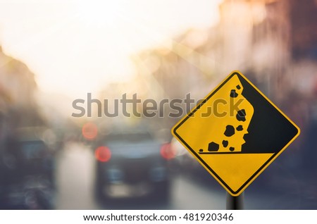 Falling stone warning traffic sign on blur road with colorful bokeh light abstract background. Copy space of travel and transportation concept. Vintage tone color filter style.