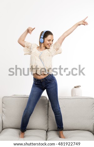 Beautiful woman at home listening music and dancing over the couch
