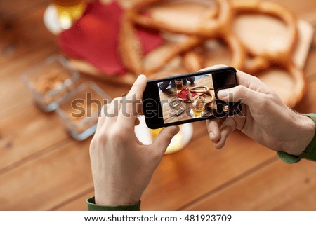 people and technology concept - close up of hands with smartphone picturing beer and pretzel at bar or pub