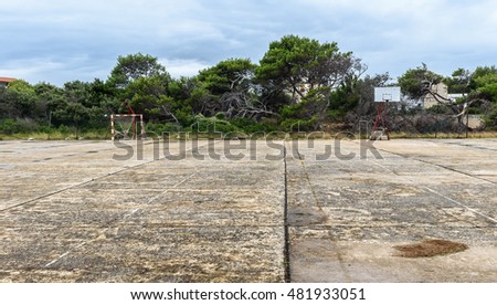 Old abandoned school sports court or schoolyard for different activities. Ruins of a sport venue abandoned long time ago with soccer, handball or football goals, basketball hoops and boards destroyed
