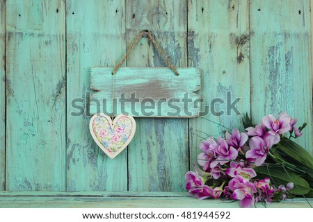 Blank wood sign with floral heart by purple flowers hanging on antique rustic mint green wooden background