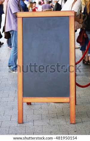 blank blackboard pavement sign with unrecognizable people in the background. also known as customer stopper or sandwich board.