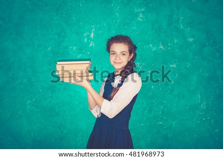 Portrait of a young schoolgirl in the form of extravagant with a briefcase or backpack. Read old books (holding a sign in her hands), bright emotion on her face. Vintage toning, Green background