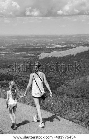 Unrecognizable mother and daughter admiring Auvergne landscape from famous dormant Puy-de-Dome volcano. France. Black and white.