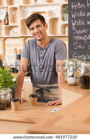 Young confident cafe worker is standing behind the countertop