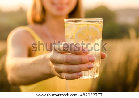 lemonade yellow vitamin energy and useful nutritional of lemon slices with lemon, lime, orange in the hand of a young girl in a yellow sports shirt on blurred background nature. Natural healthy drink.