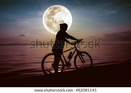 Silhouette of bicyclist in action enjoying the view at seaside on bright full moon sky background. Active outdoors lifestyle for healthy concept.