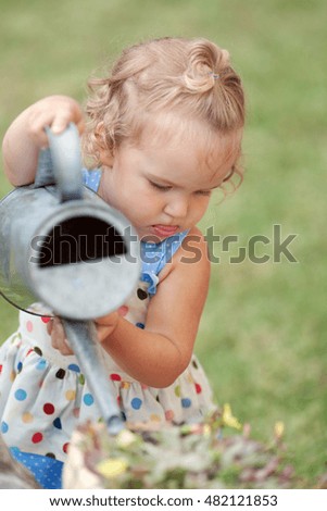 diligent cute little girl watering flowers in summer garden, outdoor