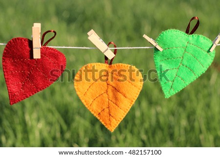 Three autumn leaf (orange, green, maroon) from fabric tissue of a pin attached to a rope on a green background