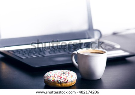 Cup of coffee with donut. In a background is computer. Coffee foam. Food, drink and technology concept. 