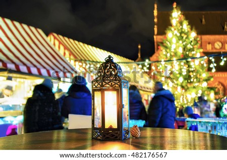 Small and bright lantern with the candle inside pictured at one of the tables at the Christmas Market in Riga, Latvia. People can find various festive goods, souvenirs, drinks and food at the market.