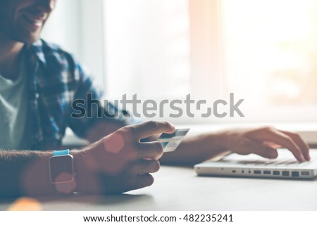 Smiling man with credit card, laptop and smart watch. Web shopping (Intentional sun glare and lens flares)