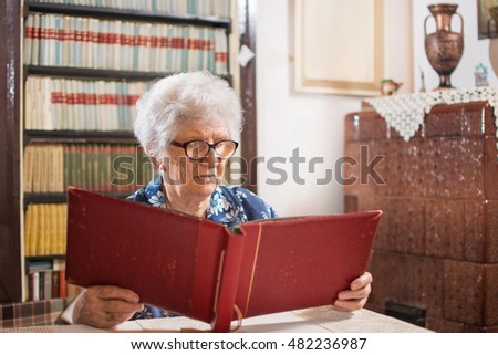Senior woman looking at photo album in living room at home.