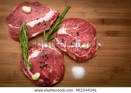 raw beef steak ribeye striploin sirloin fillet rib on wooden cutting board rosemary garlic black pepper salt