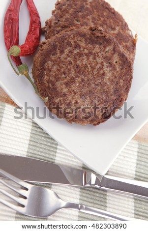 fresh juicy beef meat hamburger with dry pepper on white plate over tablecloth with cutlery