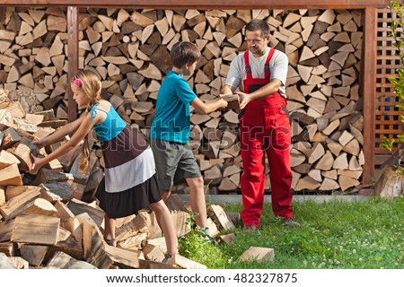 Kids helping their father to stack the chopped firewood - handing him the wood pieces
