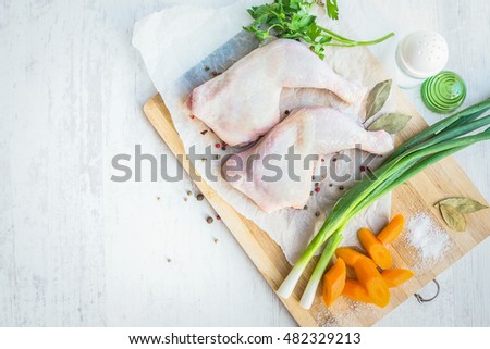 Raw chicken legs with vegetables and spices arranged on a cutting wooden board. White wood rustic background.