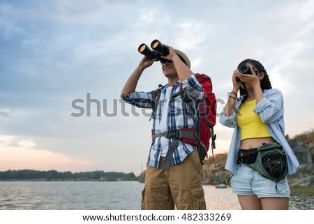 Young tourists looking at binoculars ant taking photos by lake