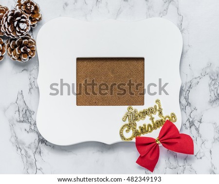 Merry christmas text on vintage white picture frame with pine cones and ribbon on white marble table top,Holiday decoration mock up.