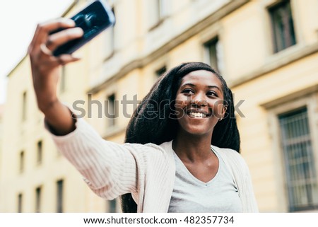 Half length of young beautiful aafro black woman outdoor in the city holding a smart phone taking selfie - technology, vanity, social network concept