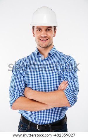 Happy handsome young man builder in hard hat standing with arms crossed over white background
