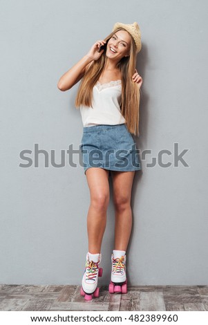 Beautiful charming girl in hat and roller skates talking on the phone isolated on a gray background