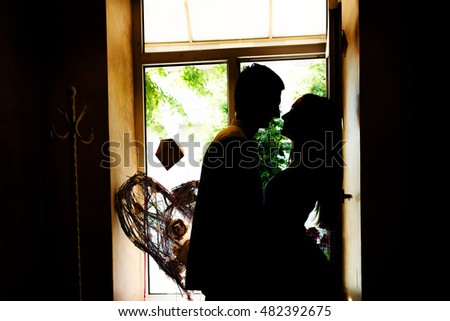 Silhouettes of the newlyweds in the cafe. A look of the loving couple standing close to each other, nose to nose, window making shadows of them