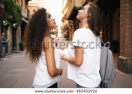 Back view of the two beautiful hipster girls walking in the city while having rest. A waist up photo of the friends wearing casual clothes while looking at the interesting places in the city.