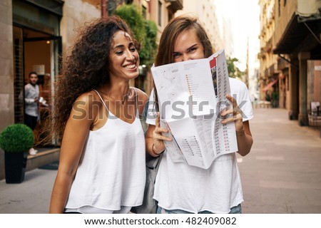 A waist up photo of the two attractive girls with long hairs exploring a new city during the trip. Friends backpa?kers wearing casual clothes are using map to find interesting places while traveling.