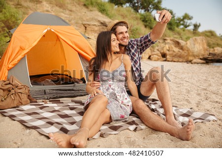 Happy young couple making selfie with smartphone and having fun camping at the beach